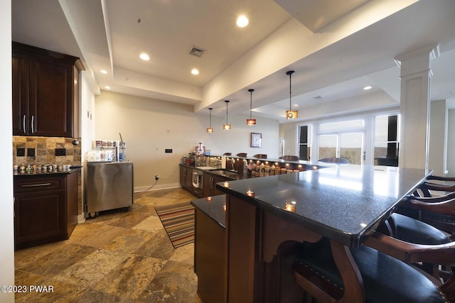 kitchen with a kitchen bar, pendant lighting, decorative columns, and a raised ceiling