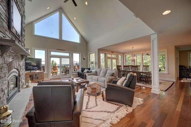 living room with ornate columns, high vaulted ceiling, wood-type flooring, a fireplace, and ceiling fan with notable chandelier