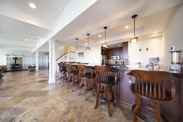 kitchen with kitchen peninsula, appliances with stainless steel finishes, a raised ceiling, pendant lighting, and a breakfast bar area