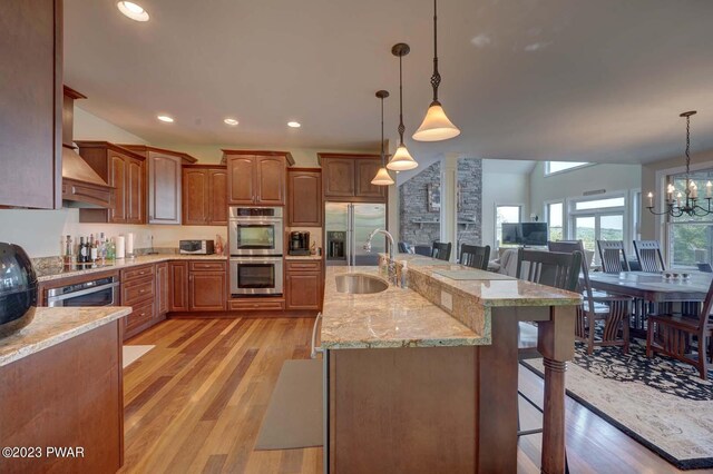 kitchen with appliances with stainless steel finishes, light wood-type flooring, a breakfast bar, sink, and hanging light fixtures