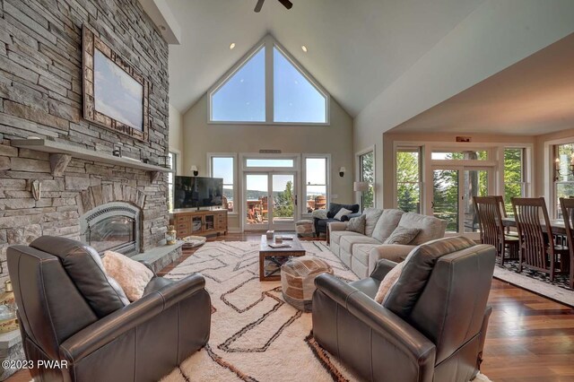 living room featuring a stone fireplace, high vaulted ceiling, a healthy amount of sunlight, and hardwood / wood-style flooring