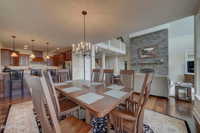 dining space with a stone fireplace, dark hardwood / wood-style flooring, and an inviting chandelier