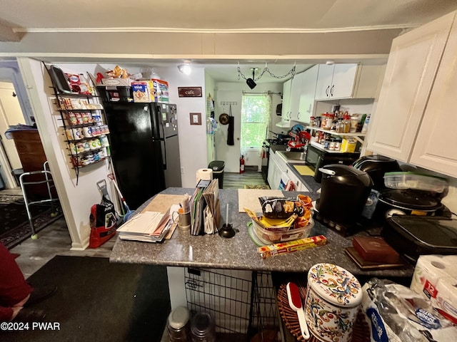 kitchen with hardwood / wood-style flooring, black fridge, white cabinetry, and stove