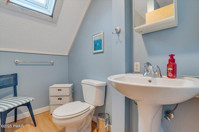 bathroom featuring wood finished floors, toilet, baseboards, a textured ceiling, and vaulted ceiling with skylight