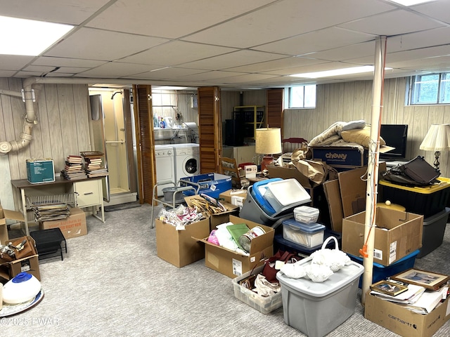 below grade area with wood walls, a drop ceiling, washing machine and clothes dryer, and carpet floors