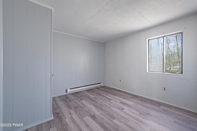 unfurnished room featuring a textured ceiling, a baseboard heating unit, wood finished floors, and brick wall