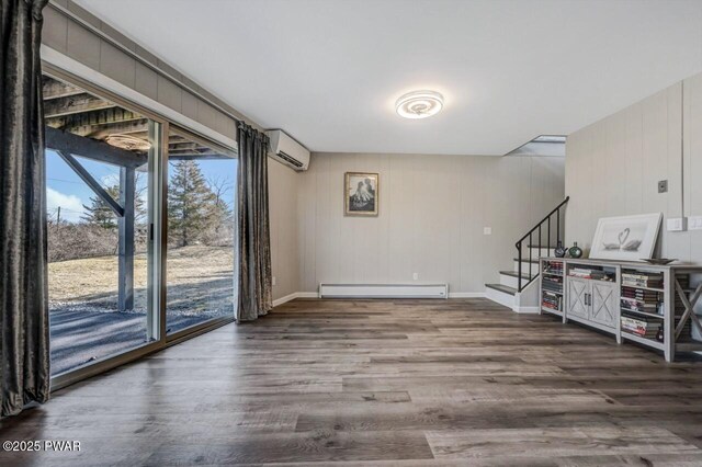 unfurnished room featuring wood finished floors, baseboards, a baseboard radiator, stairs, and a wall mounted air conditioner