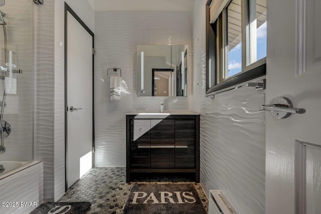 full bath with vanity, tile walls, shower / bath combination with glass door, and a baseboard radiator