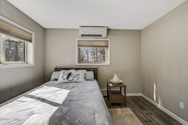 bedroom with baseboards, dark wood-type flooring, and an AC wall unit