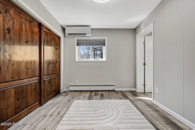 unfurnished bedroom featuring a baseboard heating unit, light wood-style flooring, baseboards, and a wall mounted air conditioner