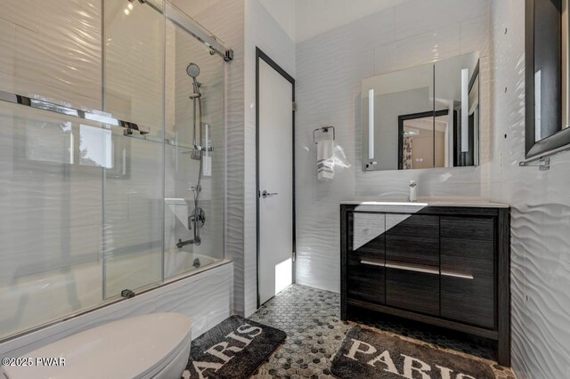 full bathroom with enclosed tub / shower combo, toilet, tile walls, and vanity