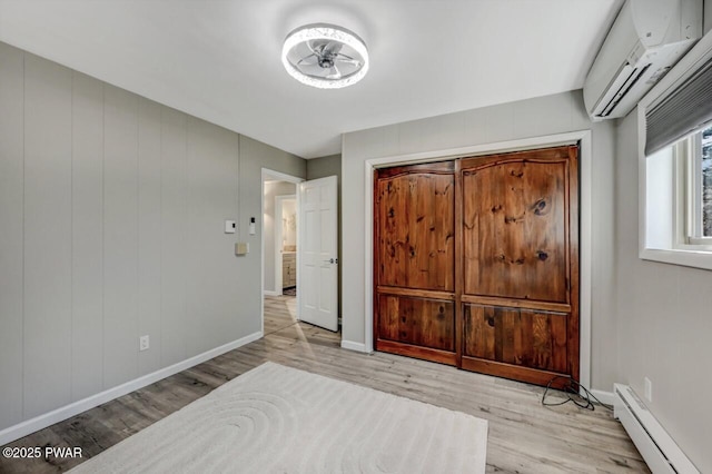 bedroom featuring a wall mounted air conditioner, a baseboard heating unit, baseboards, and wood finished floors