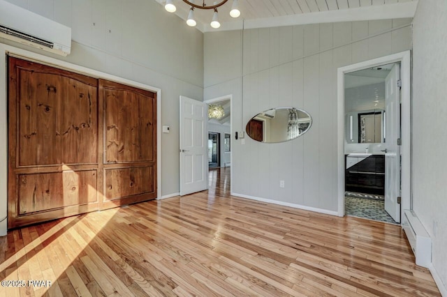 unfurnished bedroom featuring ensuite bath, an AC wall unit, light wood-style floors, and baseboards