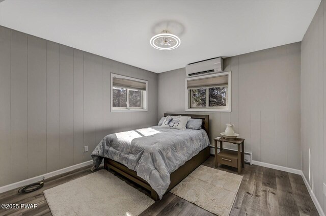 bedroom with a baseboard heating unit, an AC wall unit, wood finished floors, and baseboards