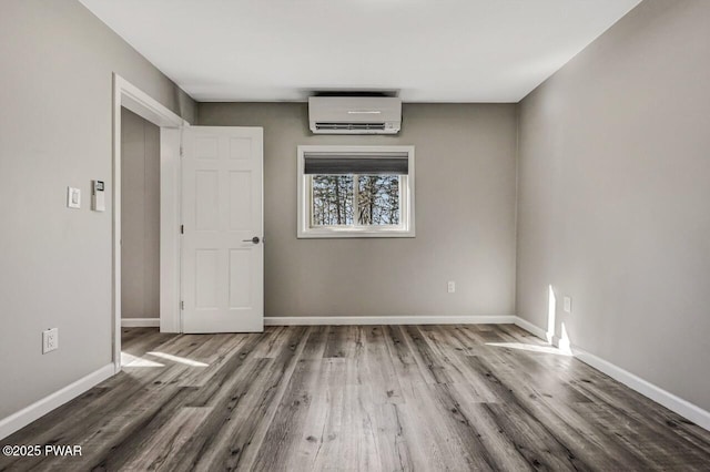 unfurnished room featuring baseboards, wood finished floors, and a wall unit AC