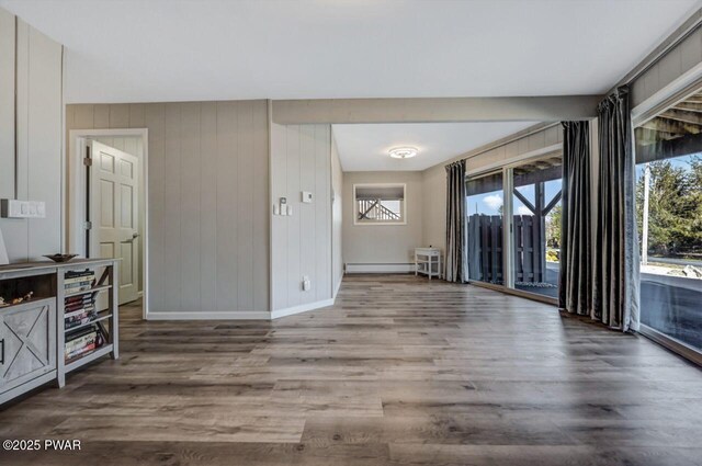 empty room with plenty of natural light, wood finished floors, baseboards, and a baseboard radiator