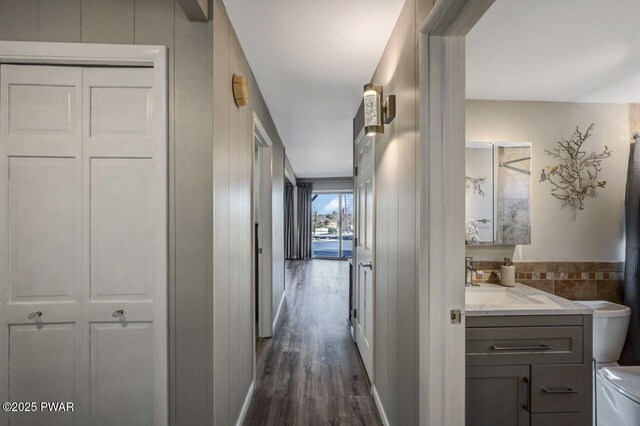 hall featuring tile walls, dark wood-style flooring, and a sink