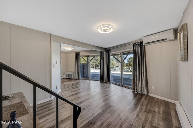 unfurnished room with wood finished floors, an AC wall unit, baseboards, and a baseboard radiator