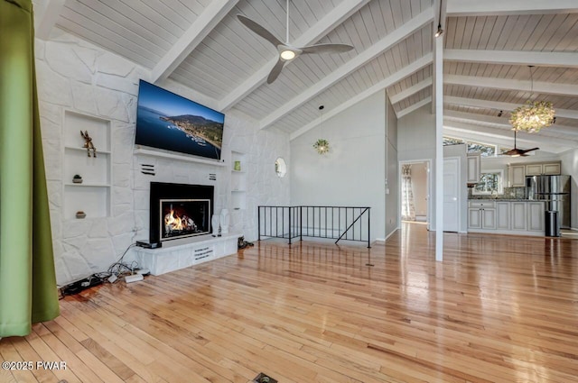 unfurnished living room featuring beam ceiling, a stone fireplace, light wood-style flooring, and a ceiling fan