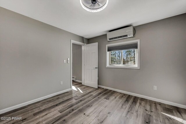 unfurnished bedroom featuring a wall mounted air conditioner, a baseboard radiator, baseboards, and wood finished floors