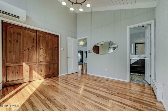 unfurnished bedroom featuring a notable chandelier, an AC wall unit, vaulted ceiling with beams, and light wood finished floors