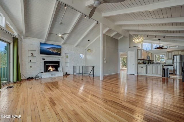 unfurnished living room featuring ceiling fan with notable chandelier, a fireplace, and light wood-type flooring