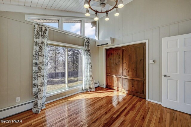 interior space with vaulted ceiling with beams, a wall mounted air conditioner, an inviting chandelier, hardwood / wood-style flooring, and a baseboard radiator