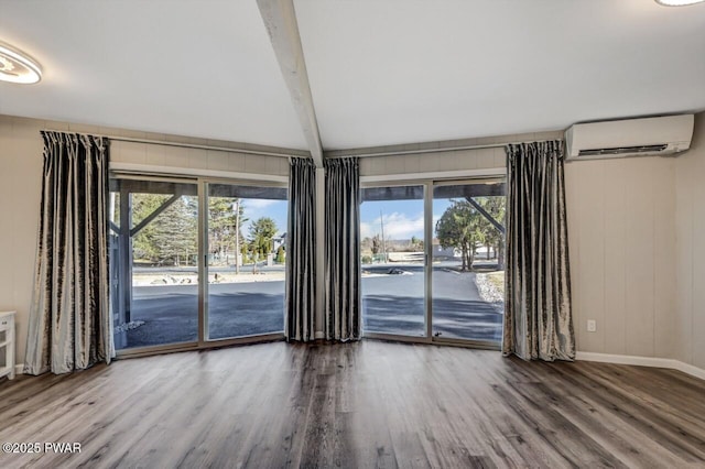 interior space featuring beam ceiling, an AC wall unit, baseboards, and wood finished floors