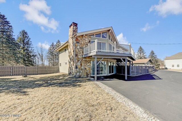 view of front of house with a wooden deck, stone siding, a chimney, and fence