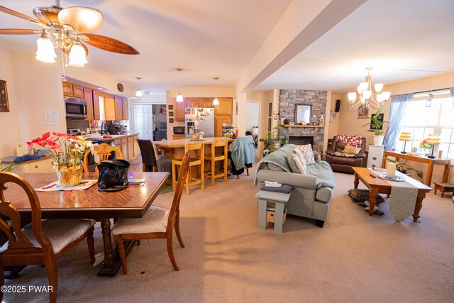 dining space featuring light colored carpet, a ceiling fan, and a stone fireplace