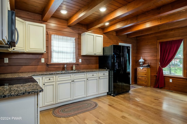 kitchen featuring beamed ceiling, wood walls, black fridge, and sink