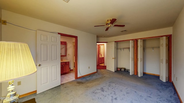 unfurnished bedroom with baseboards, visible vents, carpet floors, ensuite bath, and two closets