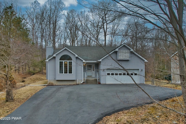 view of front facade with a shingled roof, a garage, driveway, and a chimney