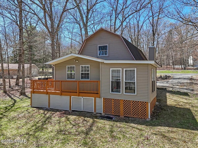 back of property featuring a yard, a gambrel roof, a chimney, and a wooden deck