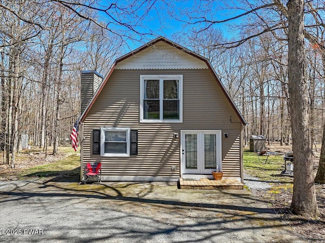 back of house with a gambrel roof, french doors, and a chimney