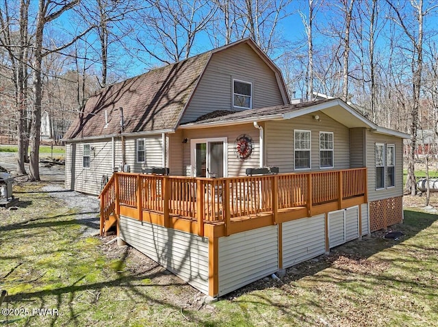 rear view of property featuring a gambrel roof, roof with shingles, and a wooden deck