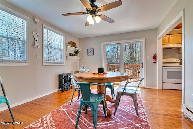 dining area with baseboards, a ceiling fan, a wood stove, and light wood-style flooring
