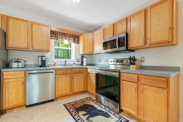 kitchen with stainless steel appliances, a sink, light brown cabinets, and light countertops