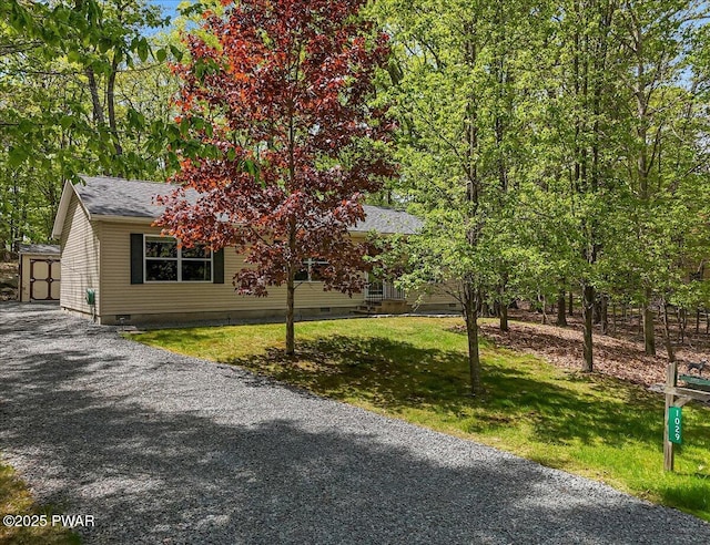 view of property hidden behind natural elements featuring crawl space, an outdoor structure, a shingled roof, and a front yard