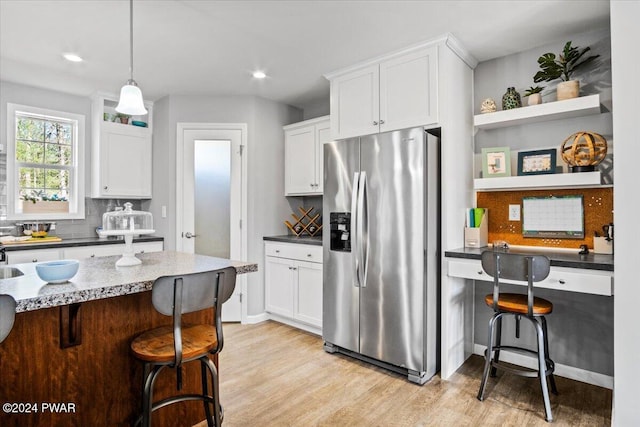 kitchen with pendant lighting, stainless steel fridge with ice dispenser, a breakfast bar area, and white cabinets