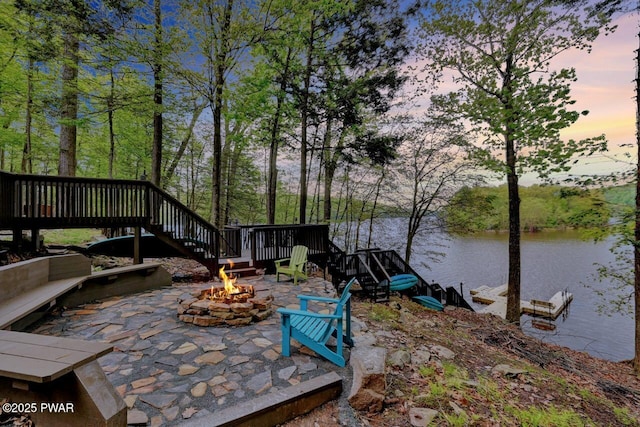 patio terrace at dusk featuring a fire pit, stairs, and a water view