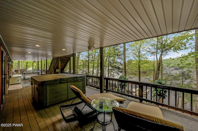 wooden terrace with a hot tub, outdoor dining space, and view of wooded area