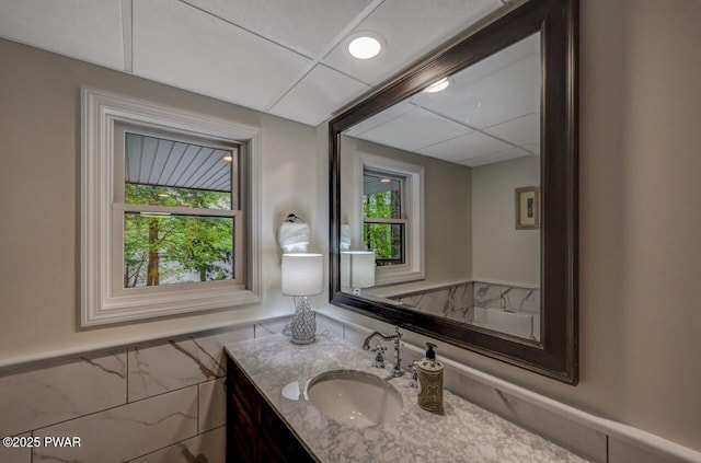bathroom with healthy amount of natural light, a wainscoted wall, vanity, and tile walls