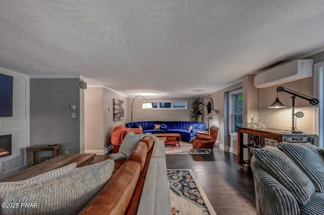 living area featuring an AC wall unit, a warm lit fireplace, wood finished floors, baseboards, and a textured ceiling