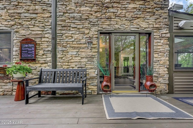 view of exterior entry with stone siding and a wooden deck