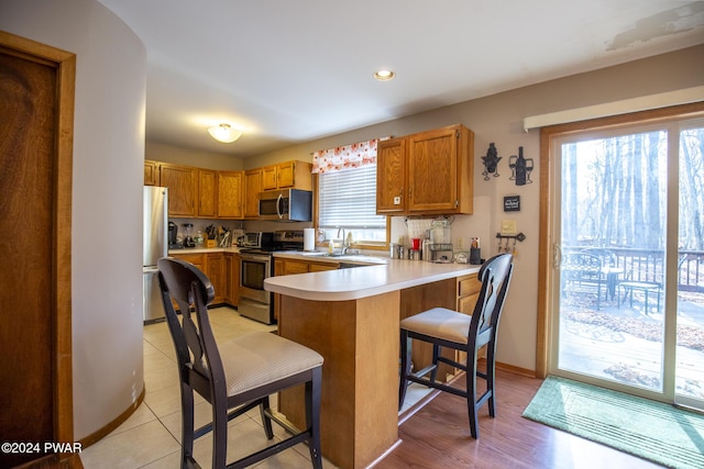 kitchen with kitchen peninsula, a breakfast bar, stainless steel appliances, sink, and light tile patterned flooring