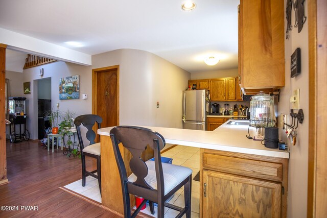 kitchen with kitchen peninsula, stainless steel fridge, and hardwood / wood-style floors