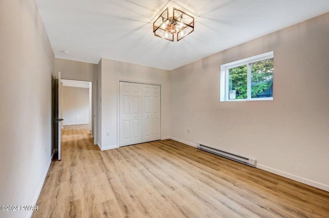 unfurnished bedroom featuring baseboard heating, a closet, and light hardwood / wood-style flooring