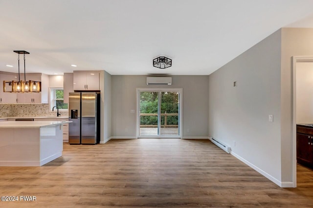 kitchen featuring a wall mounted air conditioner, a baseboard heating unit, sink, hanging light fixtures, and stainless steel fridge with ice dispenser