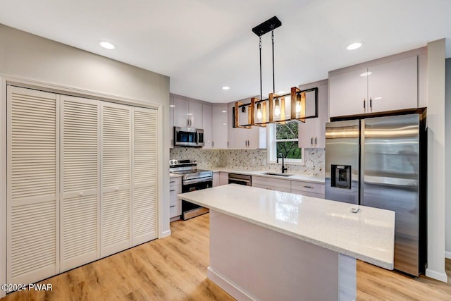 kitchen featuring sink, stainless steel appliances, light hardwood / wood-style floors, decorative light fixtures, and a kitchen island